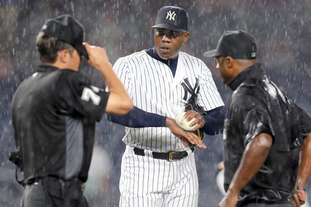 Jun 27, 2016; Bronx, NY, USA; New York Yankees relief pitcher Aroldis Chapman (54) attempts to dry his hand with the rosin bag while discussing a rain delay with home plate umpire John Tumpane (74) and third base umpire Alan Porter during the ninth inning against the Texas Rangers at Yankee Stadium. Mandatory Credit: Brad Penner-USA TODAY Sports