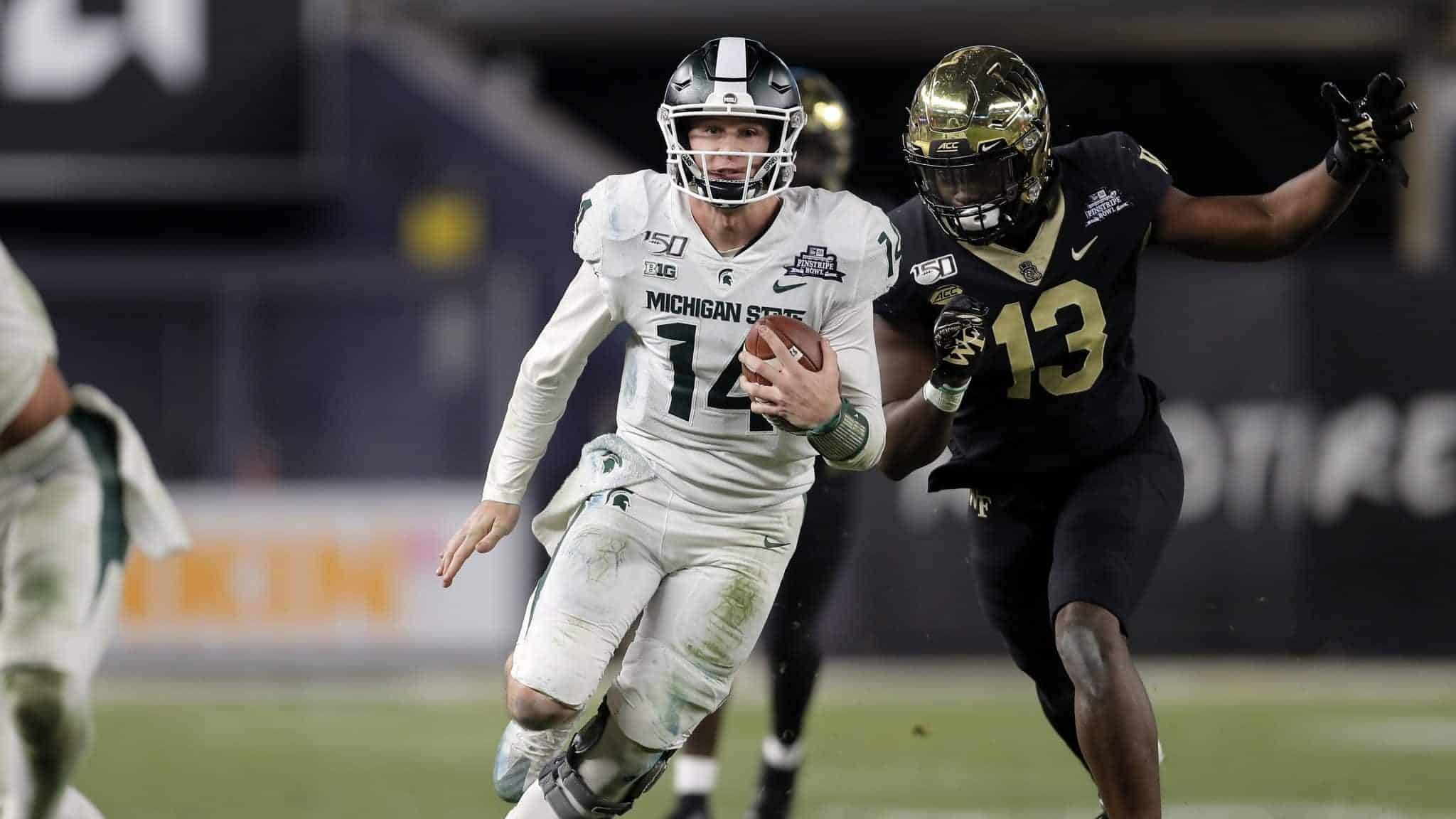 NEW YORK, NY - DECEMBER 27: Quarterback Brian Lewerke #14 of the Michigan State Spartans rushes past defensive lineman Manny Walker #13 of the Wake Forest Demon Deacons during the second half of the New Era Pinstripe Bowl at Yankee Stadium on December 27, 2019 in the Bronx borough of New York City. Michigan State Spartans won 27-21.