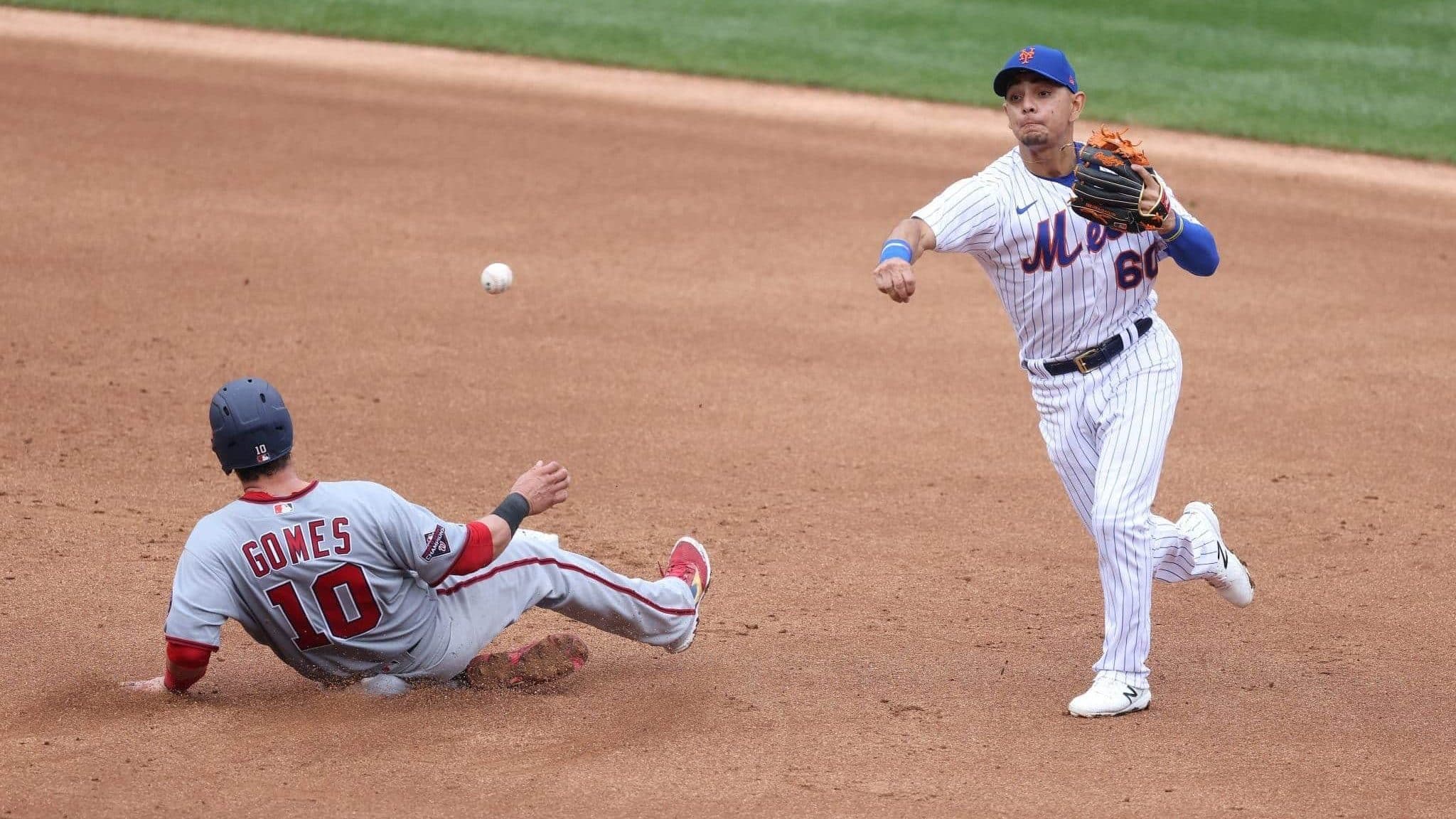 NEW YORK, NEW YORK - AUGUST 13: Andres Gimenez #60 of the New York Mets attempts to turn a double play against Yan Gomes #10 of the Washington Nationals during their game at Citi Field on August 13, 2020 in New York City.